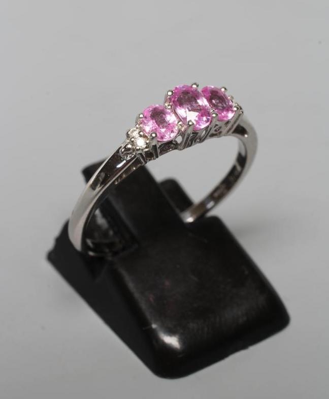 A PINK SAPPHIRE RING, the three oval facet cut stones claw set to shoulders each with two diamond Image