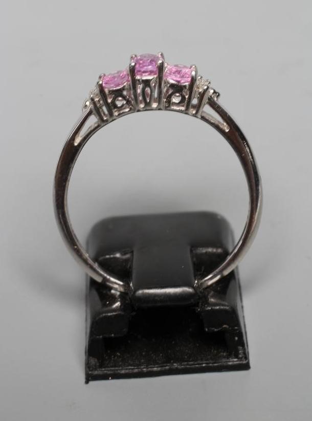 A PINK SAPPHIRE RING, the three oval facet cut stones claw set to shoulders each with two diamond Image