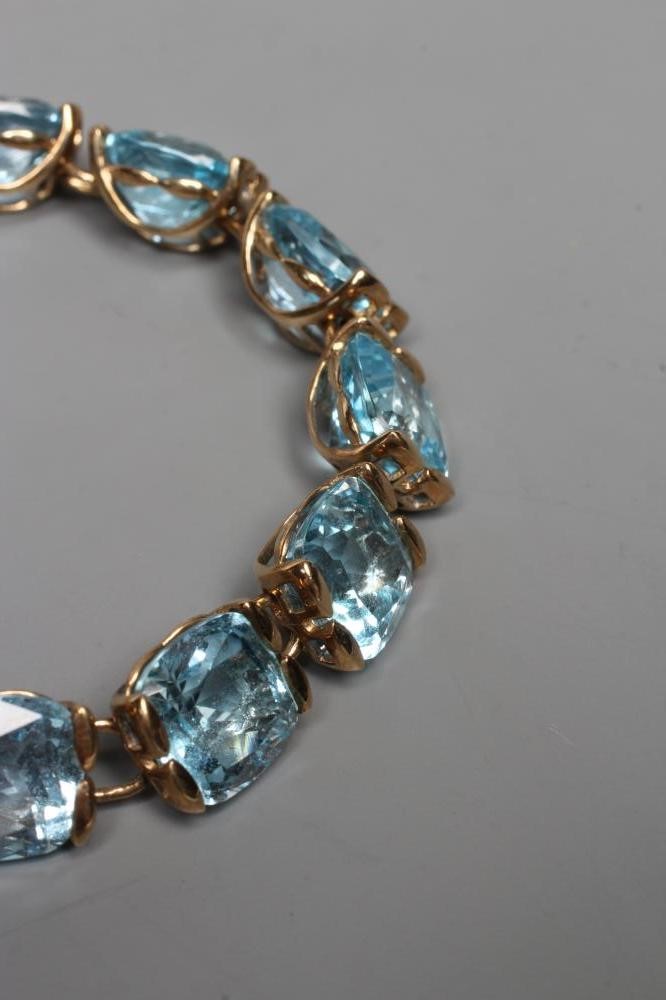 A BUE TOPAZ BRACELET, the fourteen cushion cut stones set to a plain link 9ct gold frame with slide Image