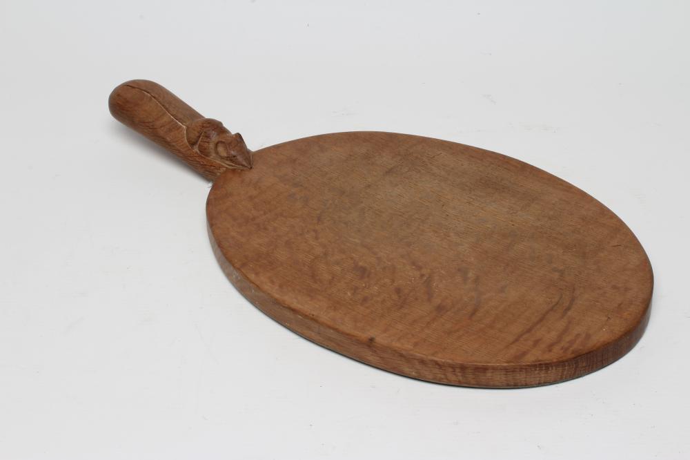 A ROBERT THOMPSON ADZED OAK CHEESE BOARD of oval form, the lug handle with carved mouse trademark in Image