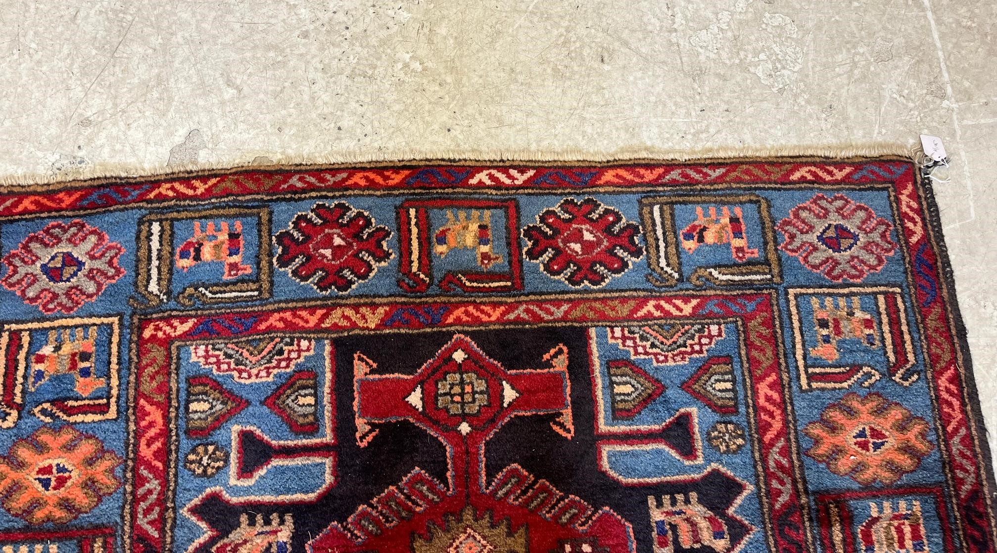 A PERSIAN STYLE WOOL RUG, modern, the black field with large claret red gul and sky blue spandrels, Image