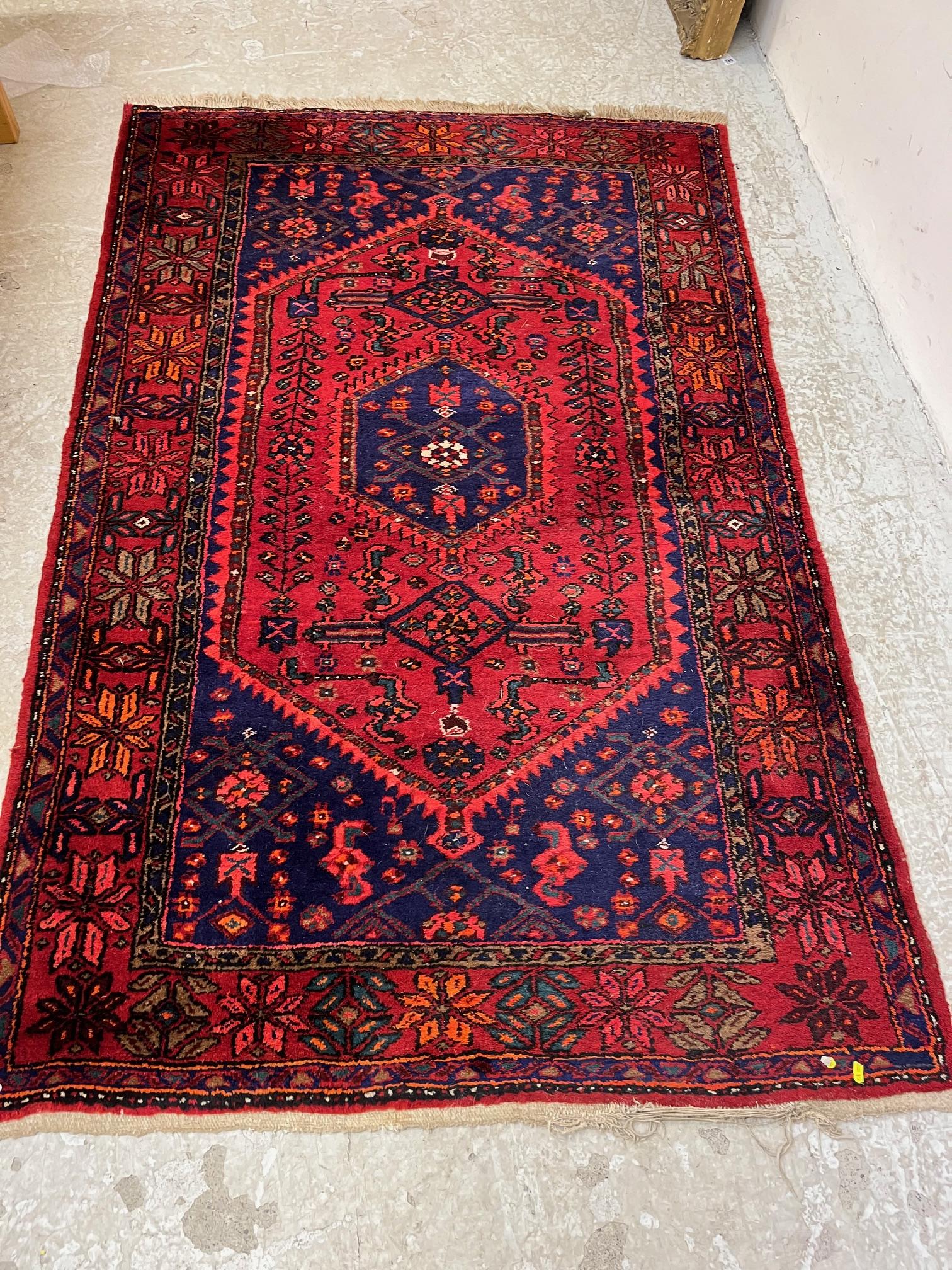 A PERSIAN STYLE WOOL RUG, modern, the burgundy floral field with indigo gul and spandrels, within a Image