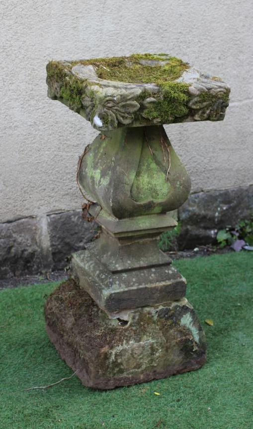 A SANDSTONE BIRD BATH, the square bowl with leaf and flower carved edge, on bulbous square stem with Image