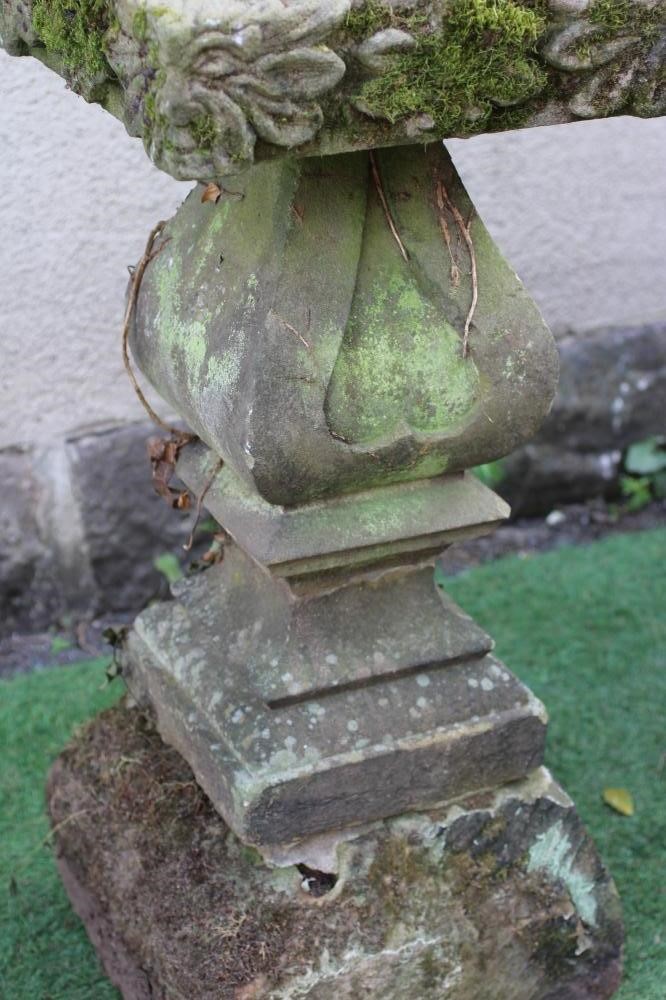 A SANDSTONE BIRD BATH, the square bowl with leaf and flower carved edge, on bulbous square stem with Image