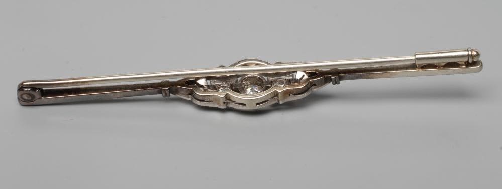 A DIAMOND BAR BROOCH centred by a collet set brilliant cut stone of approximately 0.20cts flanked by Image