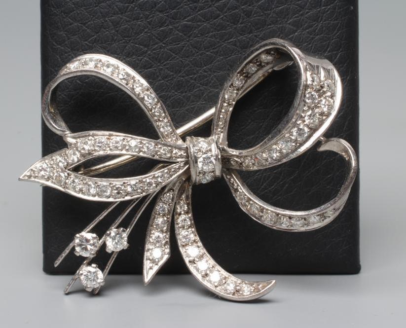 A DIAMOND BOW BROOCH, the white unmarked metal frame pave set with numerous round cut stones (Est. Image