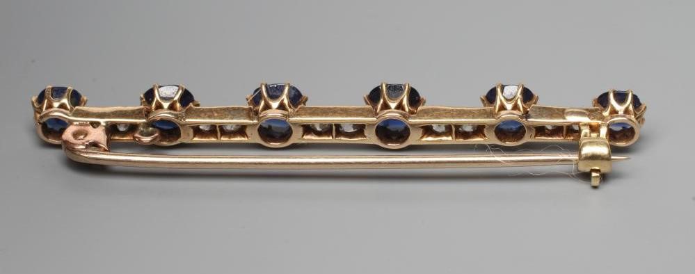 A SAPPHIRE AND DIAMOND BAR BROOCH, the six graduated circular facet cut sapphires claw set to a Image