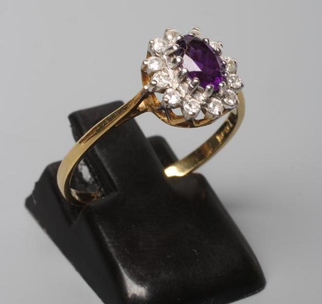 AN AMETHYST AND DIAMOND CLUSTER RING, the oval facet cut amethyst claw set to a border of small Image