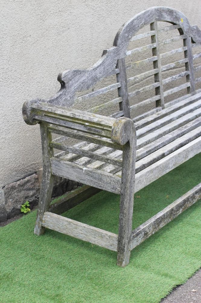 A LUTYENS STYLE SLATTED TEAK GARDEN BENCH with arched back and scrolled arms, raised on square Image