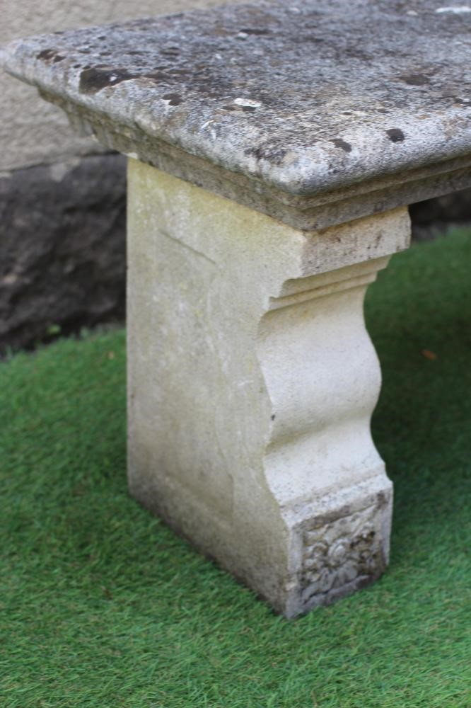 A CAST STONE BENCH, the moulded edged oblong seat raised on flower moulded square section end Image