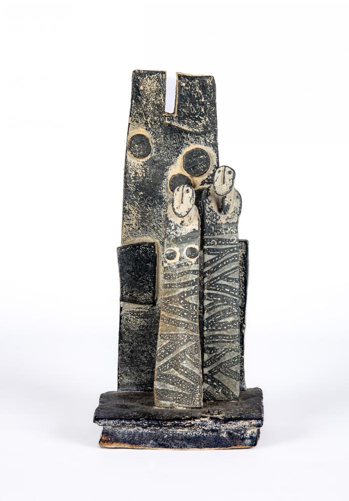 JOHN MALTBY (1936-2000) - a matt grey stoneware sculpture of two figures standing before a cut slab Image