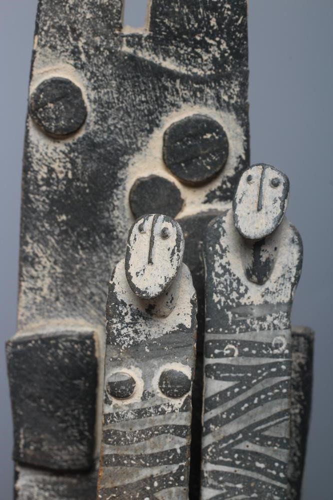 JOHN MALTBY (1936-2000) - a matt grey stoneware sculpture of two figures standing before a cut slab Image