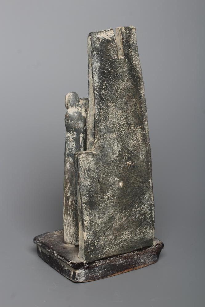 JOHN MALTBY (1936-2000) - a matt grey stoneware sculpture of two figures standing before a cut slab Image