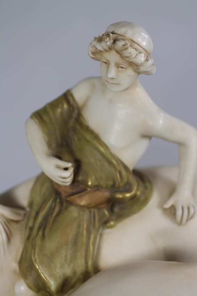 A ROYAL DUX PORCELAIN GROUP modelled as a young man wearing a green draped tunic seated astride a Image