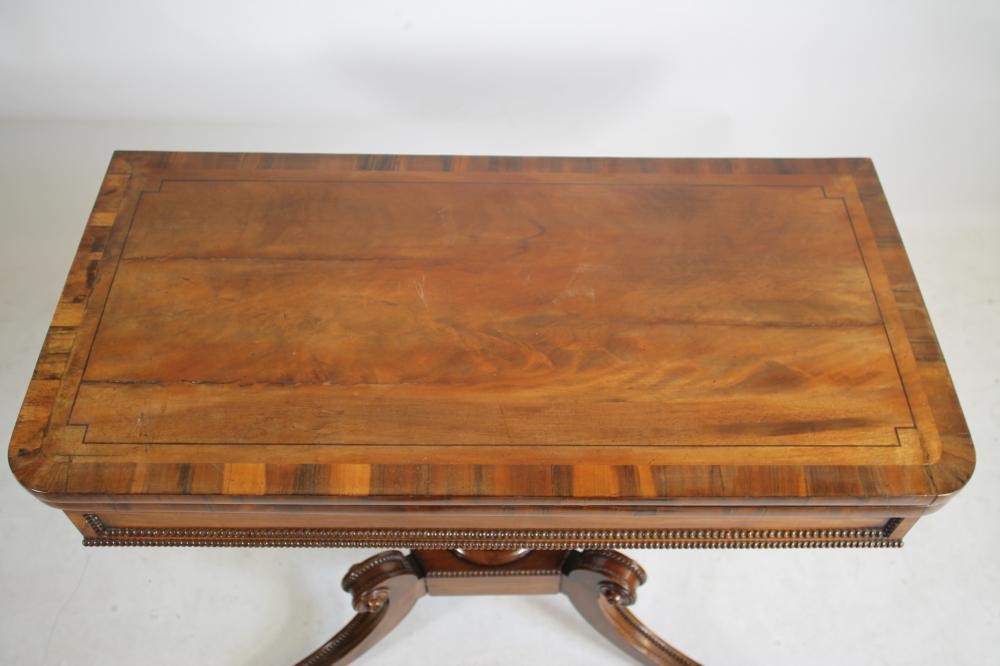 A REGENCY MAHOGANY FOLDING CARD TABLE of rounded oblong form with stringing and beaded edging Image