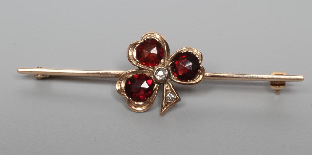 AN EDWARDIAN BAR BROOCH centred by a garnet set shamrock with diamond centre and stem Image