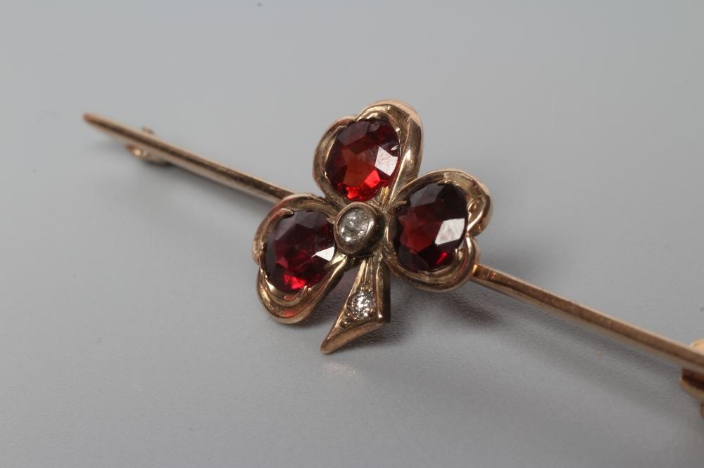 AN EDWARDIAN BAR BROOCH centred by a garnet set shamrock with diamond centre and stem Image