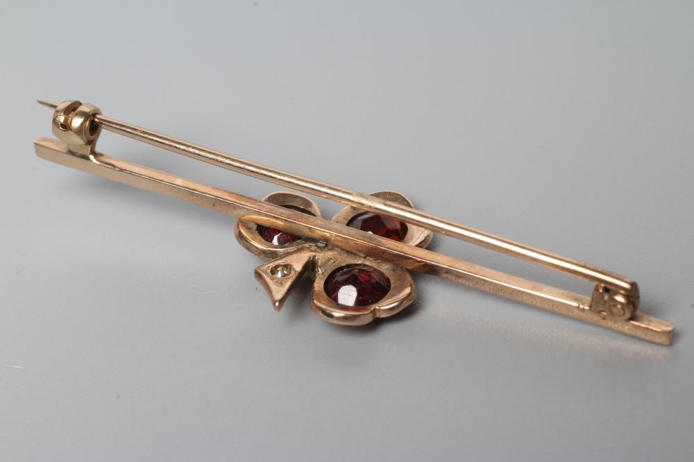 AN EDWARDIAN BAR BROOCH centred by a garnet set shamrock with diamond centre and stem Image