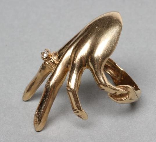 A 9CT GOLD COCKTAIL RING shaped as a lady's left hand wearing a diamond solitaire "ring" Image