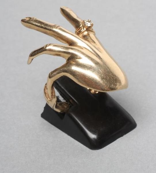A 9CT GOLD COCKTAIL RING shaped as a lady's left hand wearing a diamond solitaire "ring" Image