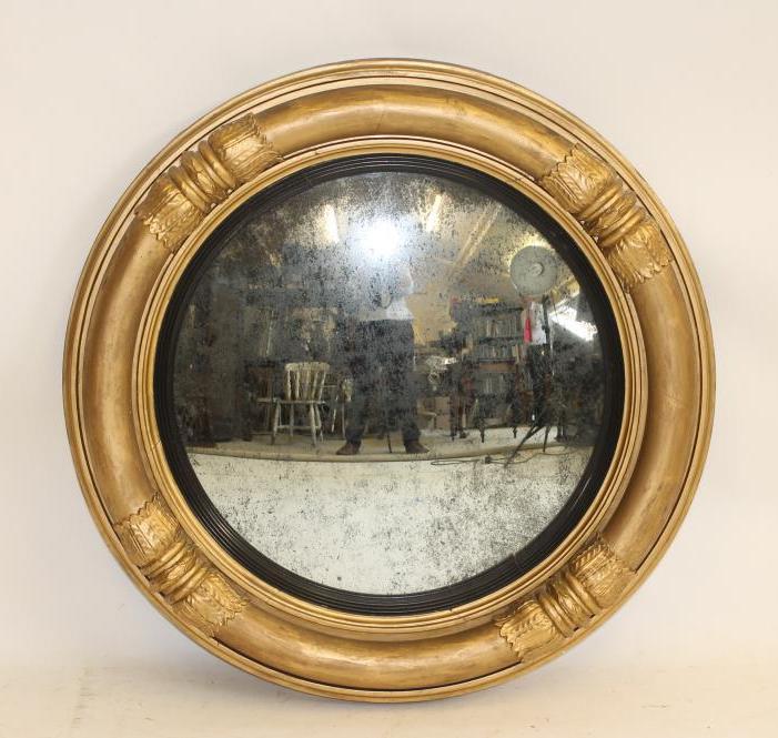 A REGENCY GILT WOOD CONVEX MIRROR with reeded slip and leaf clasped pole frame Image