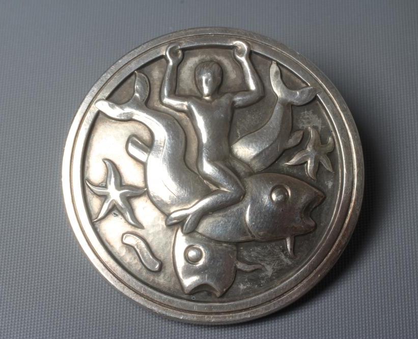 A GEORG JENSEN SILVER CIRCULAR BROOCH designed by Arno Malinowski with a merman riding on the back Image