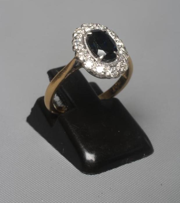 A SAPPHIRE AND DIAMOND CLUSTER RING, the oval facet cut sapphire claw set to a border of small pave Image