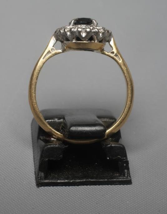 A SAPPHIRE AND DIAMOND CLUSTER RING, the oval facet cut sapphire claw set to a border of small pave Image