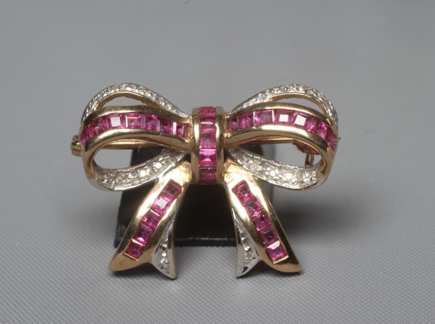 A RUBY AND DIAMOND BOW BROOCH channel set with numerous small square cut rubies and pave set diamond Image