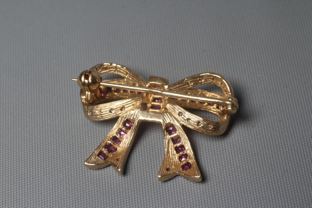 A RUBY AND DIAMOND BOW BROOCH channel set with numerous small square cut rubies and pave set diamond Image