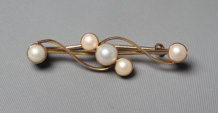 AN EDWARDIAN BROOCH peg set with five graduated cultured pearls on a scroll knife edge bar, applied Image