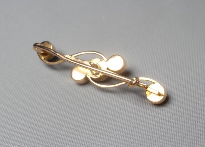 AN EDWARDIAN BROOCH peg set with five graduated cultured pearls on a scroll knife edge bar, applied Image
