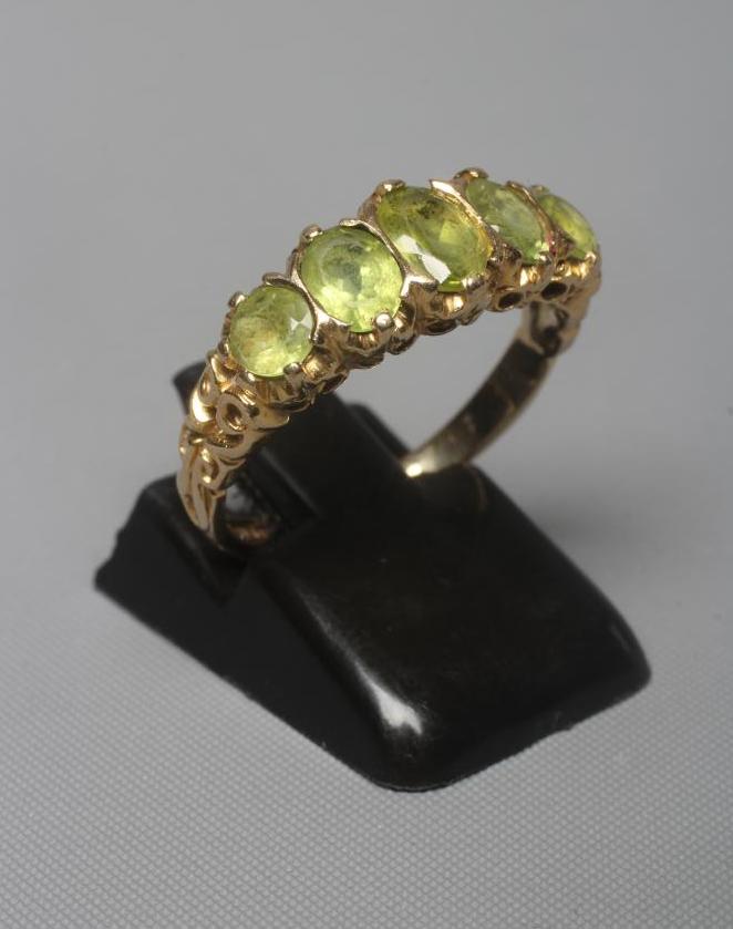 A VICTORIAN STYLE PERIDOT RING, the five mix cut stones claw set to carved shoulders and a plain 9ct Image