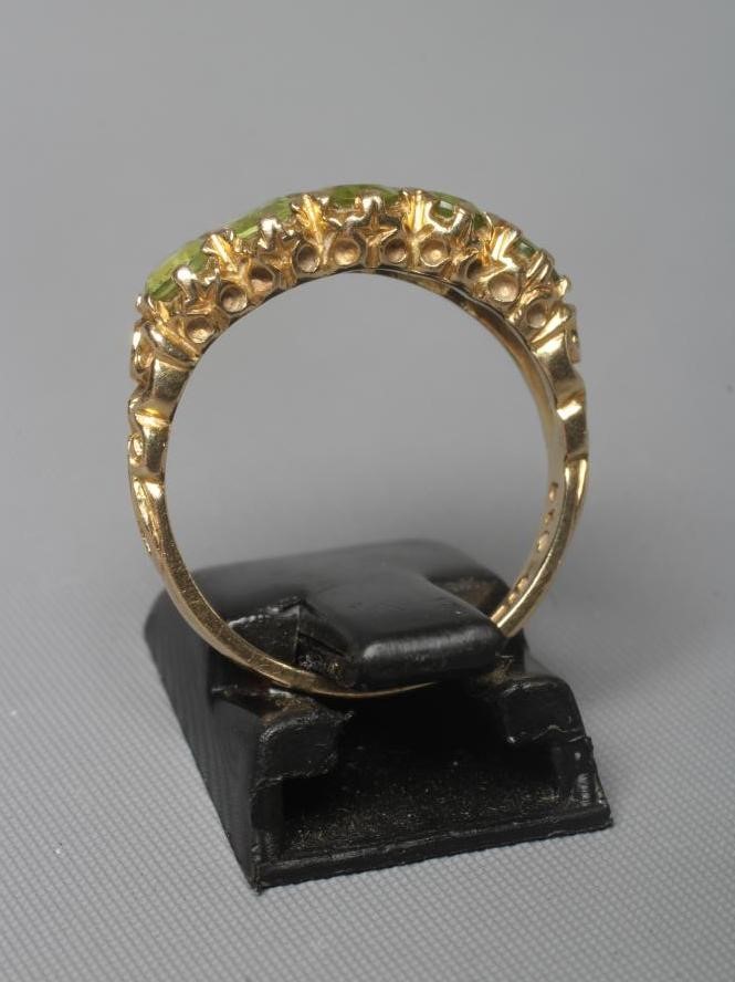 A VICTORIAN STYLE PERIDOT RING, the five mix cut stones claw set to carved shoulders and a plain 9ct Image