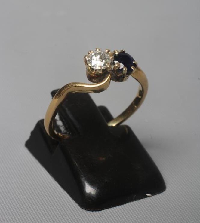 A TWO STONE SAPPHIRE AND DIAMOND CROSSOVER RING, the two facet cut stones claw set to a plain shank Image