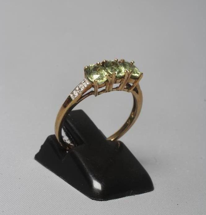 A THREE STONE PERIDOT RING, the oval facet cut stones claw set to shoulders each point set with two Image