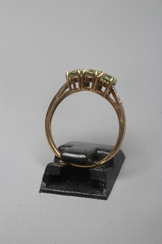 A THREE STONE PERIDOT RING, the oval facet cut stones claw set to shoulders each point set with two Image