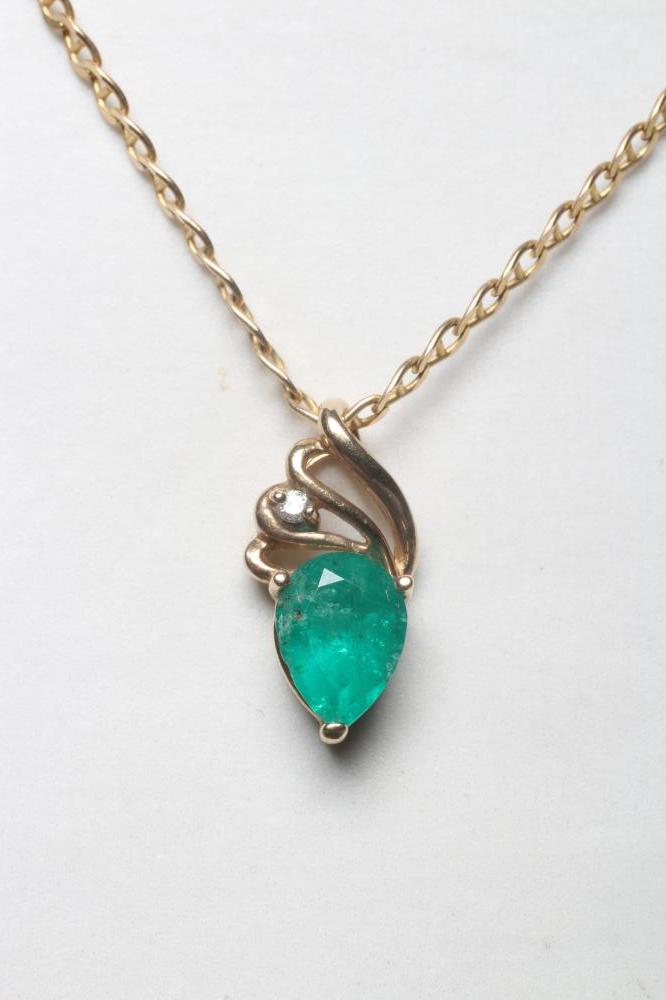 AN EMERALD PENDANT, the triangular facet cut stone claw set to an open scroll bale claw set with a Image