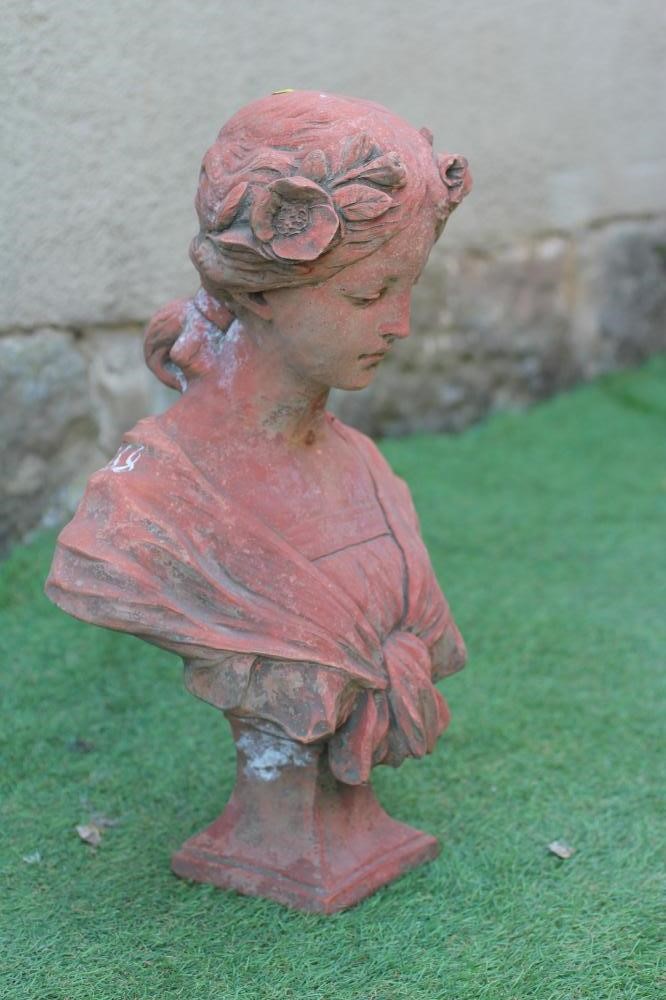 A TERRACOTTA BUST OF A YOUNG MAIDEN modelled with flowers in her tied-up hair, on waisted square Image