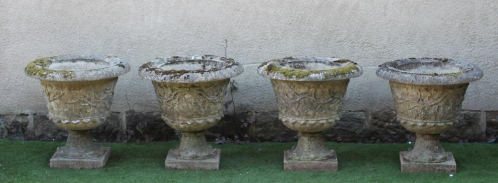 A SET OF FOUR CAST STONE URNS with everted rim over a body with trailing vine, on waisted leaf Image