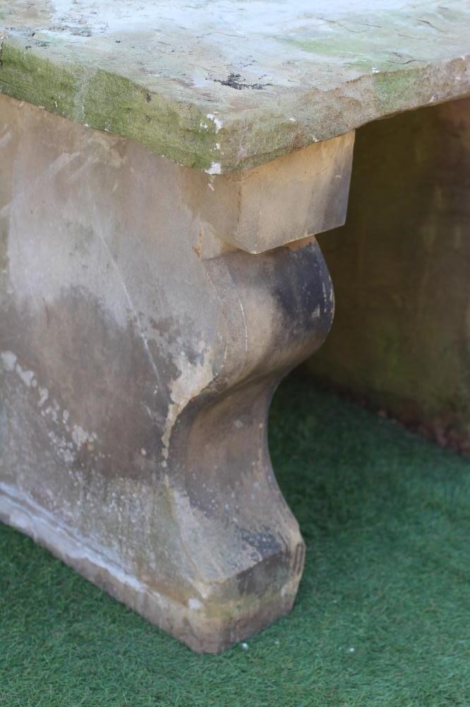 A SANDSTONE BENCH, the oblong seat with rough-hewn edge raised on square section scrolled fronted Image