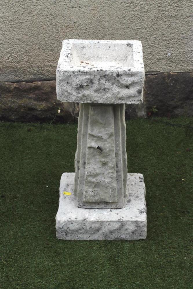 A COMPOSITION STONE BIRD BATH of rusticated square form raised on tapering panelled stem Image