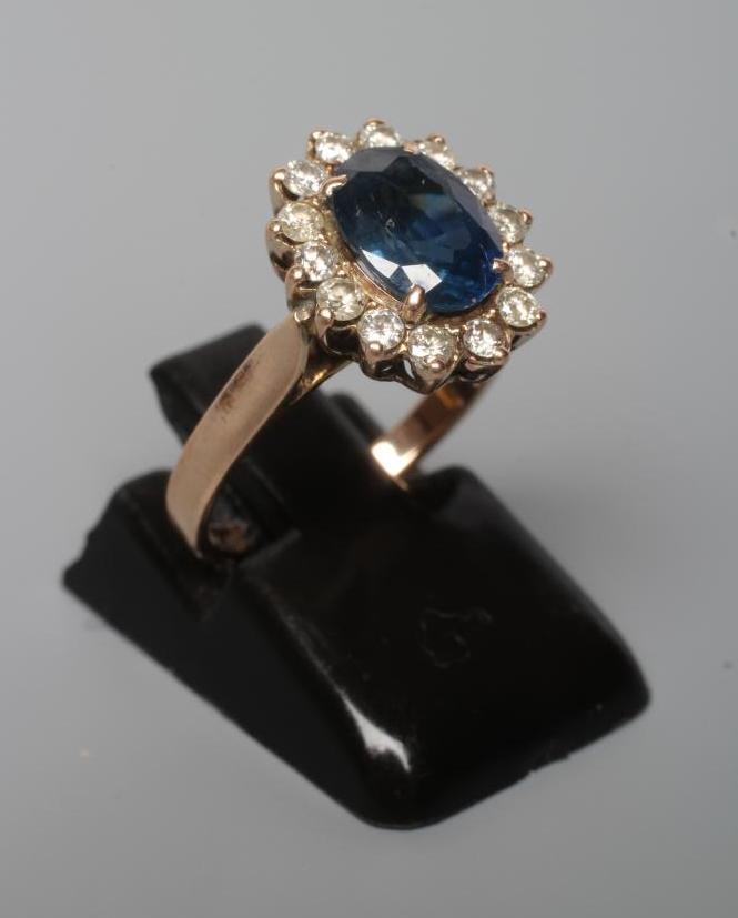 A SAPPHIRE AND DIAMOND CLUSTER RING, the oval facet cut sapphire claw set to a border of fourteen Image