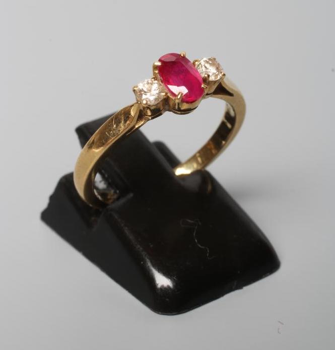A RUBY AND DIAMOND THREE STONE RING, the central oval facet cut ruby claw set and flanked by two Image