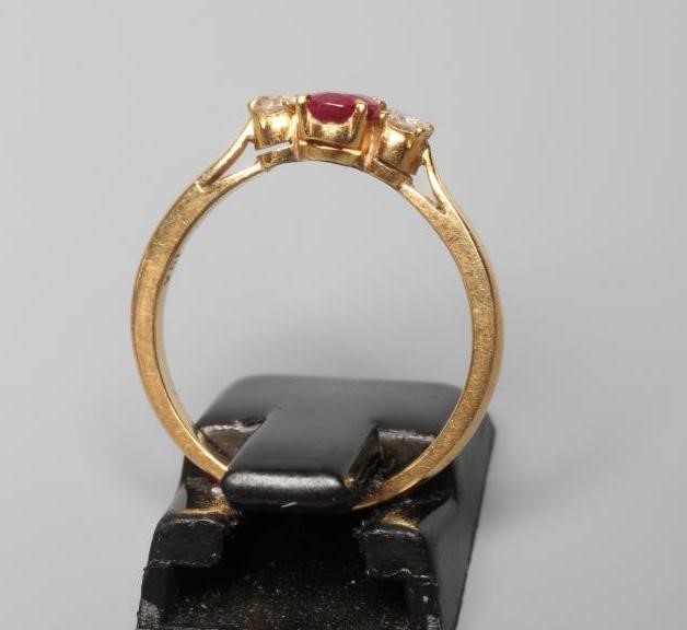 A RUBY AND DIAMOND THREE STONE RING, the central oval facet cut ruby claw set and flanked by two Image