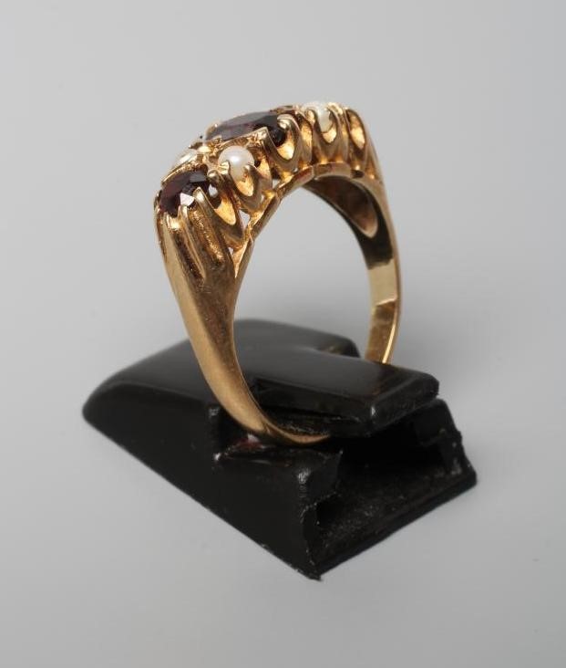 A THREE STONE GARNET RING, the facet cut stones claw set with four seed pearls between, on carved Image