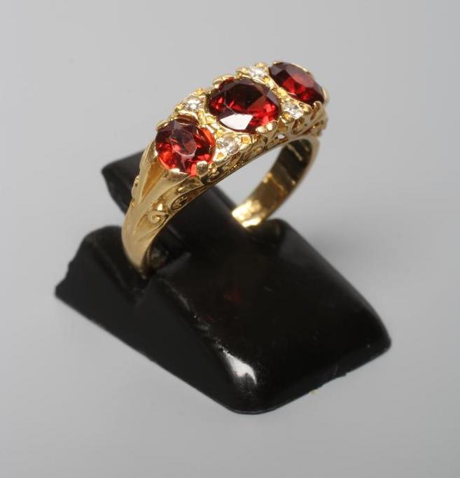 A THREE STONE GARNET RING, the facet cut stones with four diamond points between, to carved Image