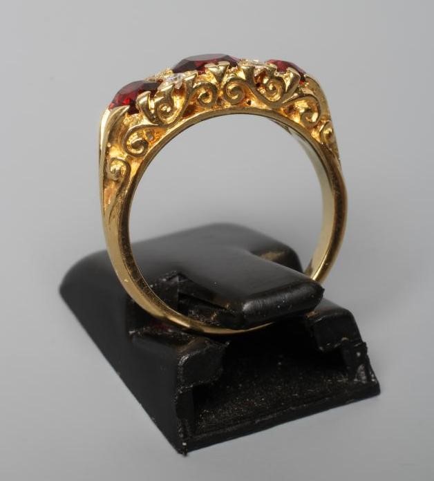 A THREE STONE GARNET RING, the facet cut stones with four diamond points between, to carved Image