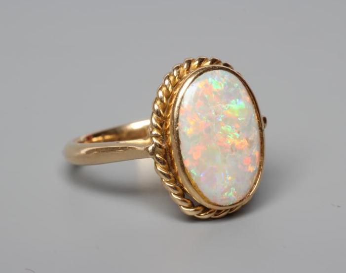 AN OPAL DRESS RING, the oval cabochon polished stone collet set to a rope twist mount and plain Image