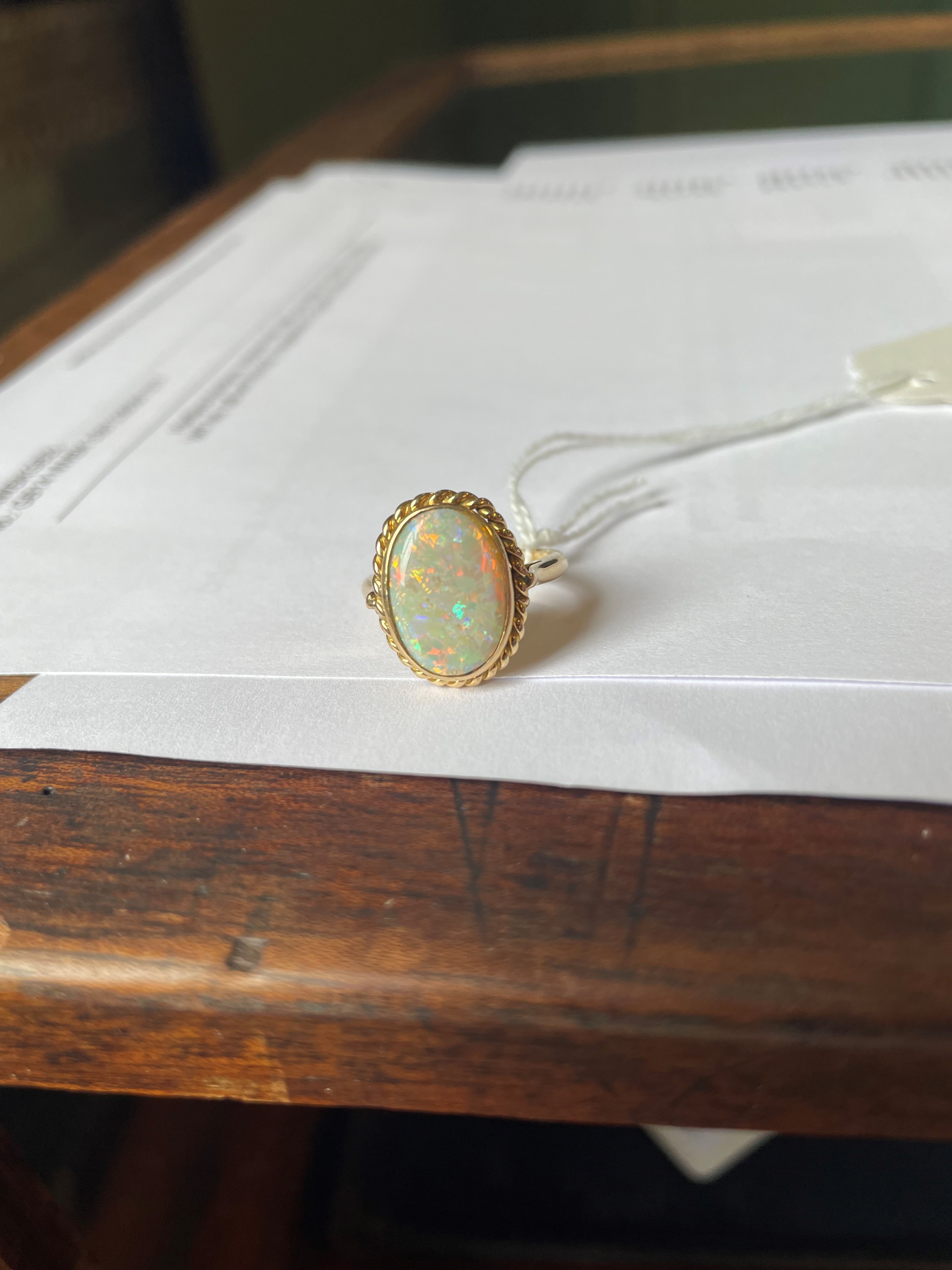 AN OPAL DRESS RING, the oval cabochon polished stone collet set to a rope twist mount and plain Image